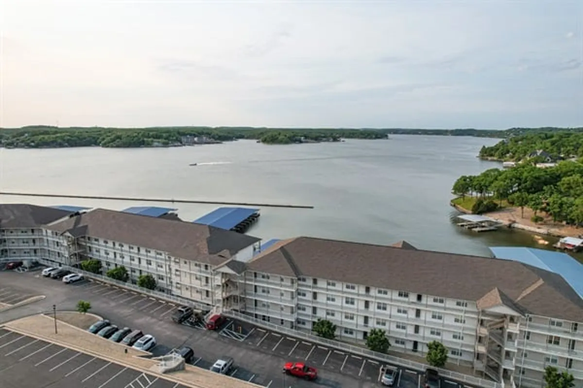 A sweeping view of the lake with boats moored nearby, a parking area for easy access, and a shoreline perfect for fishing or picnicking. The expansive water and active scene hint at the variety of water sports and lakeside activities available.