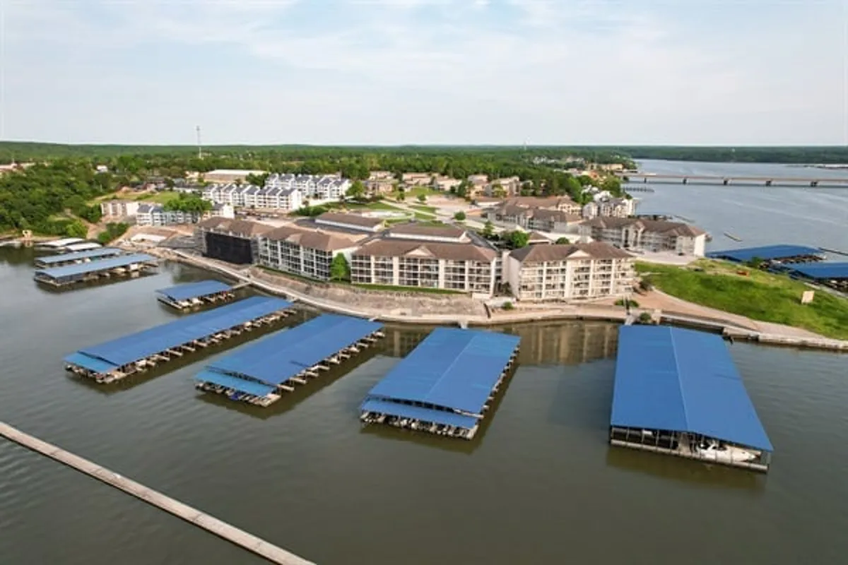 The image captures a peaceful waterfront scene at a marina dock, with residential buildings and lush greenery lining the shore. The setting sun casts a warm glow over the water, emphasizing the tranquil ambiance and boating lifestyle.