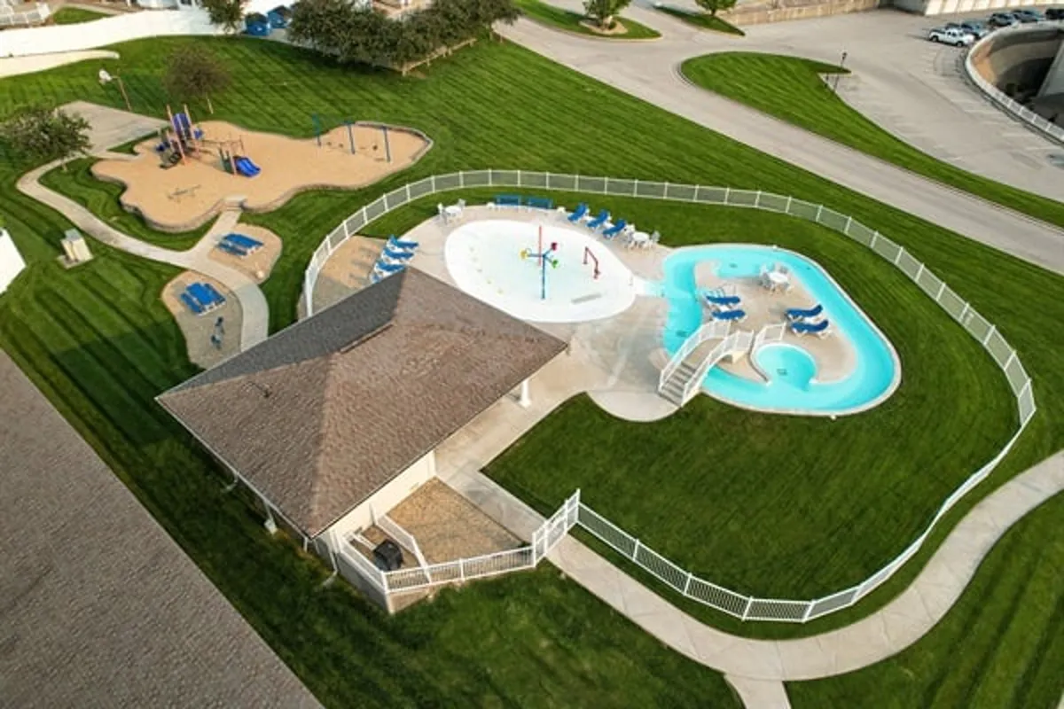 A vibrant outdoor space featuring a children's playground, splash pad, swimming pool, and a dedicated picnic area. The scene exudes energy, with children playing and families gathered for outdoor meals or celebrations.