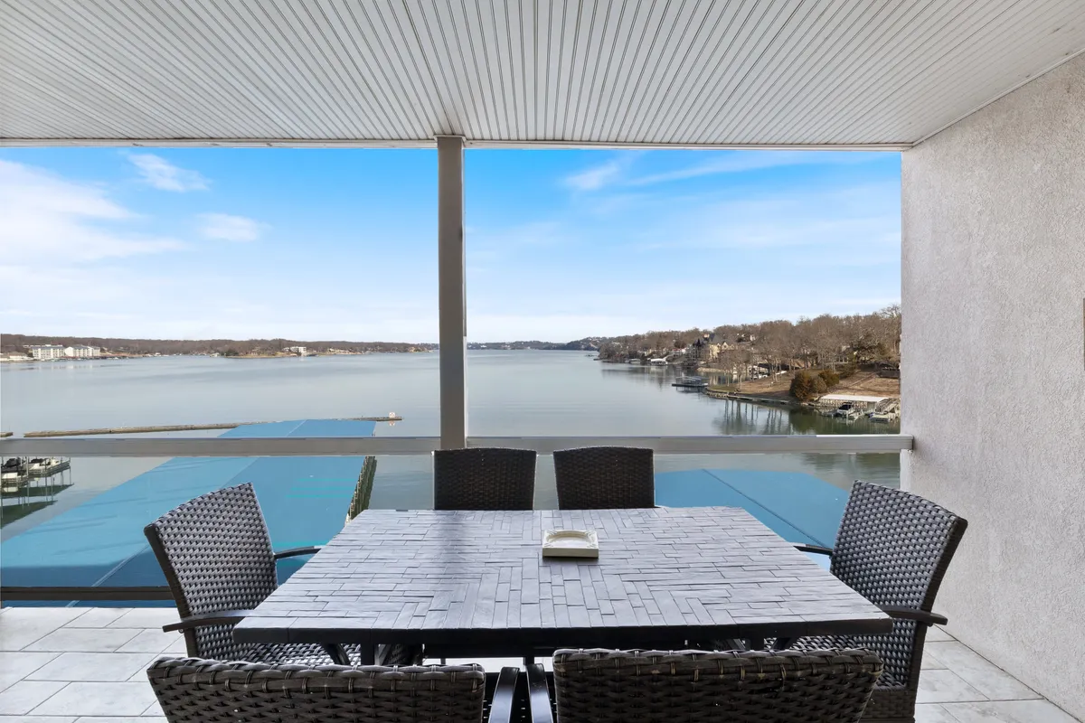 This image shows a dining table set on a private deck with a direct view of the lake. Beyond the table, you can see outdoor seating that offers a front-row seat to the water and sunrise or sunset views.