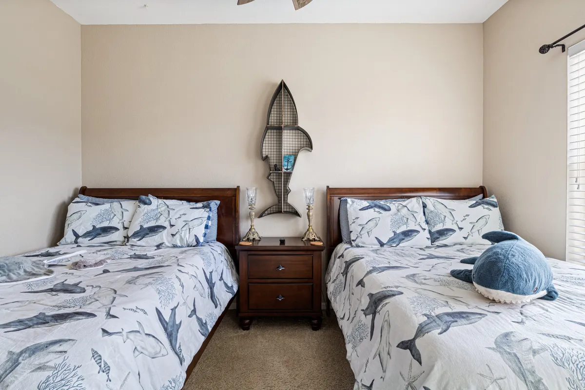 A cozy bedroom with twin beds dressed in fish-themed bedding, complemented by decorative fish wall art and a nightstand with lamps. The space feels playful yet calming, ideal for families or friends seeking a comfortable retreat.