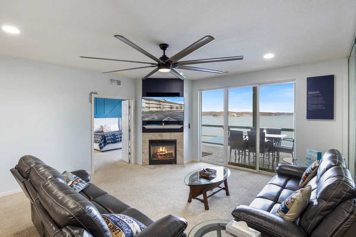 A cozy living room featuring comfortable leather sofas arranged around a modern fireplace, with large windows offering sweeping views of the lake. Nautical accents and a decorative table contribute to the welcoming atmosphere. The setting is perfect for family relaxation, socializing, or simply enjoying the sunset from inside.