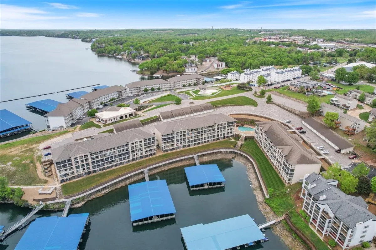 A panoramic lakefront view featuring boathouses, landscaped gardens, and residential buildings, with scenic walking trails and tranquil green spaces. The setting is calm and welcoming, inviting guests to explore the lakeside and nearby attractions.