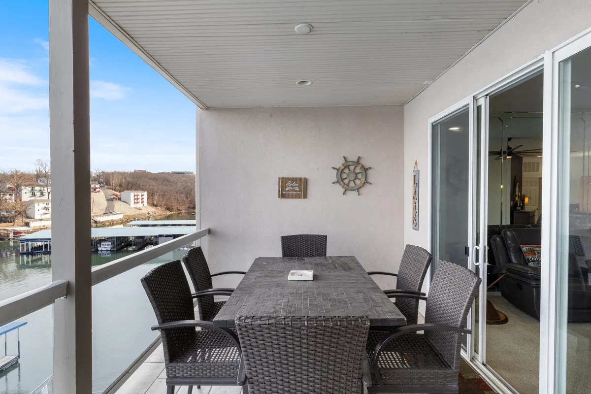 An inviting outdoor dining table set on a patio overlooking the water, with decorative wall art adding to the ambiance. The setting is ideal for al fresco dining, intimate conversations, and sunset views, capturing the essence of lakeside romance.