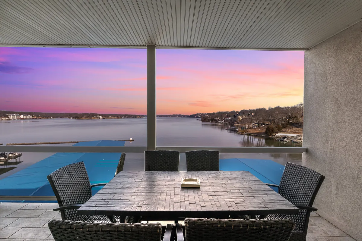 The hero image captures a spacious dining table set for gathering, positioned next to large windows or on a patio overlooking the sparkling lake at Osage Beach. The sun sets over the water, painting the sky in warm hues, inviting guests to relax, dine, and savor panoramic views with friends or family.