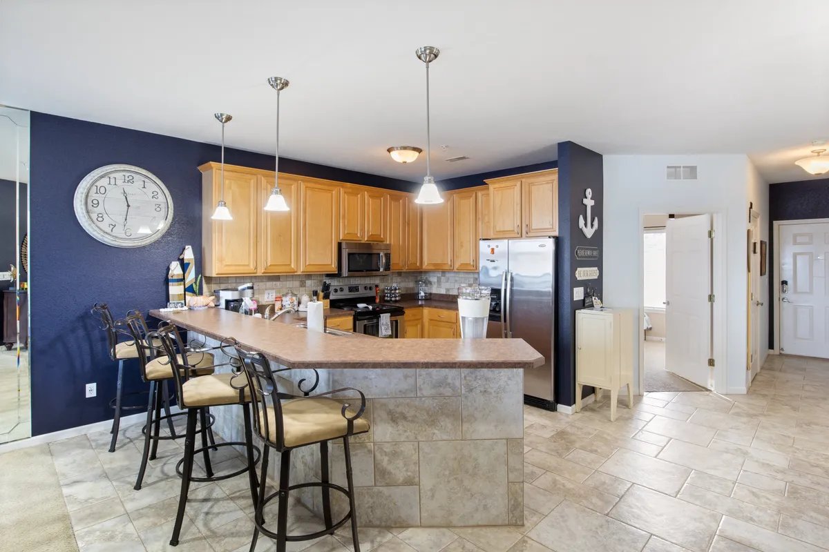 A stylish, fully stocked kitchen with a prominent island, sleek stainless steel appliances, and inviting pendant lighting. The layout encourages gathering for meal prep or casual conversation, reflecting a space designed for both culinary activity and socializing.
