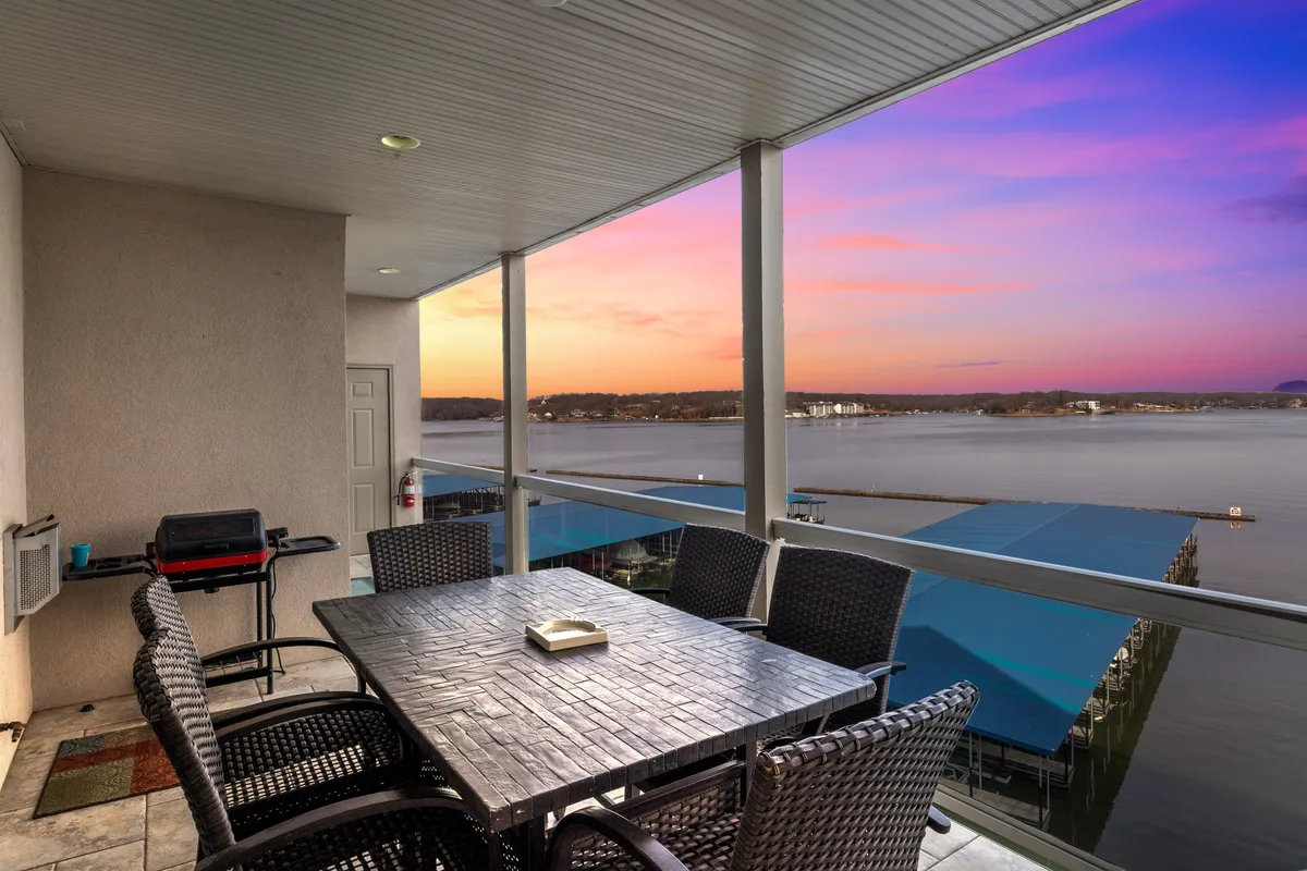 An inviting outdoor dining setup overlooking the lake, with a sunset sky providing a picturesque backdrop. The table is ready for alfresco meals, and the ambiance radiates relaxation and togetherness just steps from the indoor living spaces.